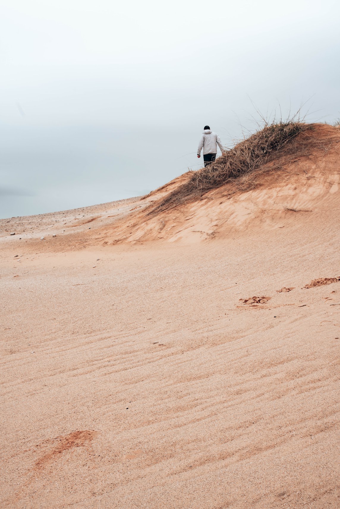A person walking across pale sand dunes